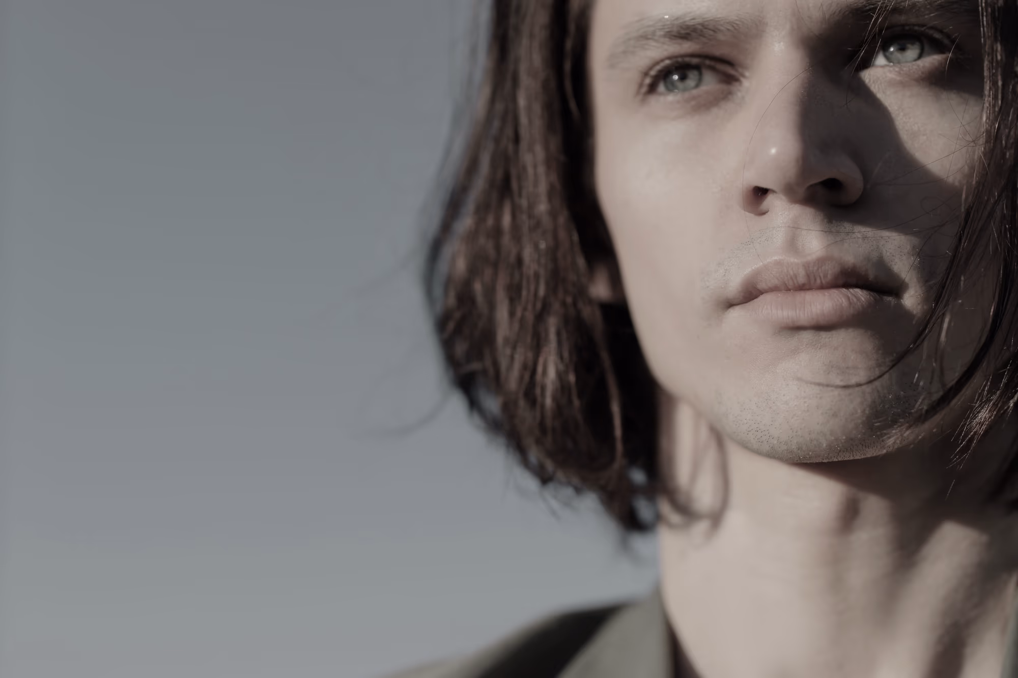 Portrait d’un jeune homme aux cheveux longs, le regard tourné vers l’horizon, sur fond de ciel