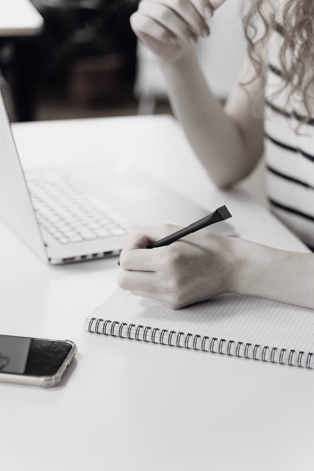 Jeune femme prenant des notes dans un carnet à côté d’un ordinateur portable